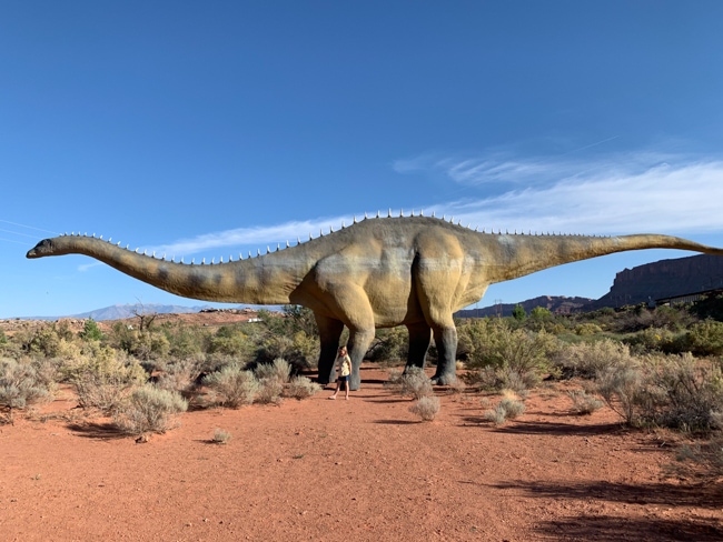 Girl standing with one of the large dinosaur models at Moab Giants