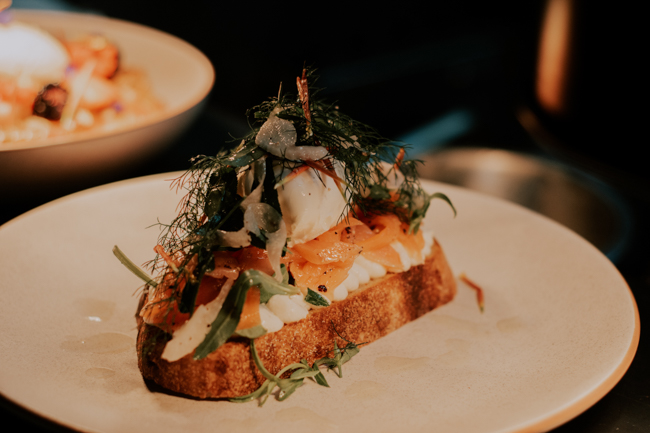 A plate featuring a trout dish stacked on top of a slice of bread covered in green garnish.