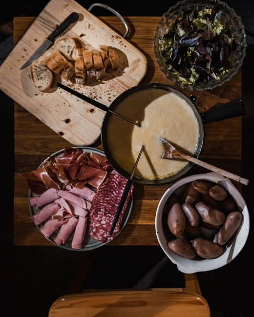 A table top featuring at The Melting Pot, one of the best Boise restaurants, featuring cheese fondue with bread, meat and vegetables to dip.