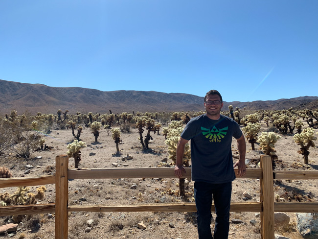 A park visitor standing in front of a wood fence with trees and moutains in Joshua Tree in December.